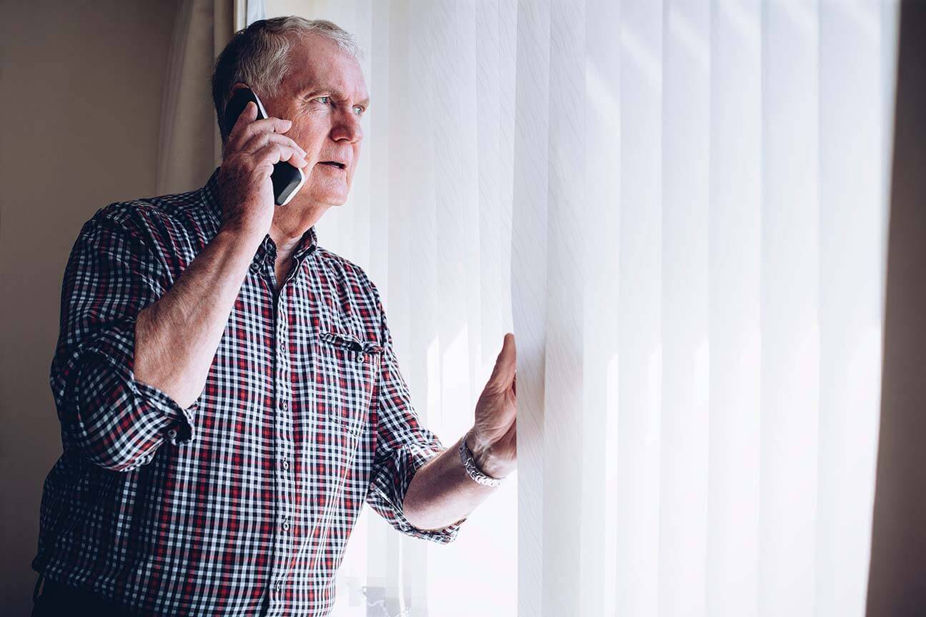 senior citizen speaking on a landline and looking out of his window