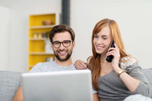man and woman speaking on a cell phone while using their laptop